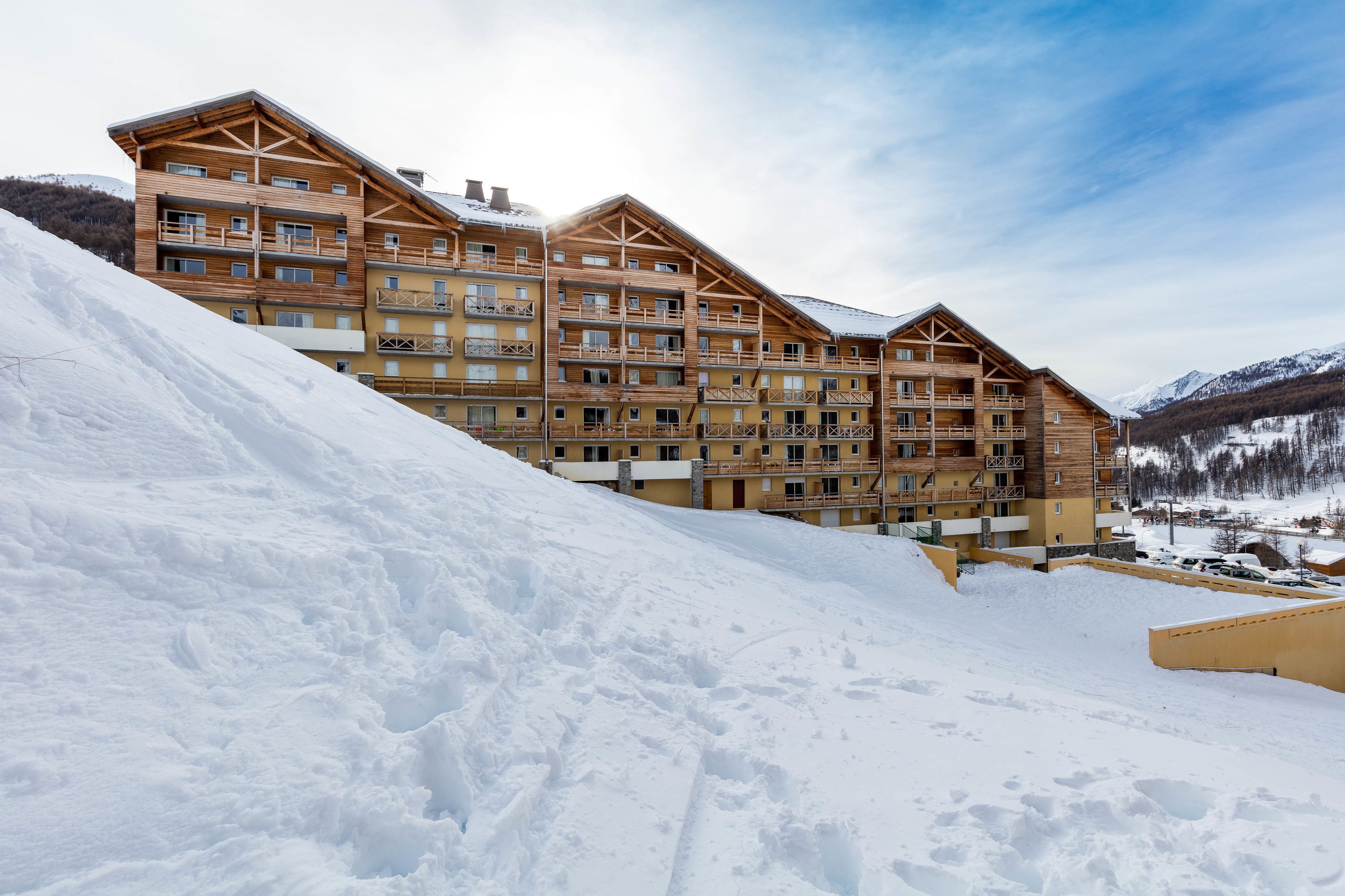 A multi-story wooden lodge with balconies, set against a snowy mountain backdrop.