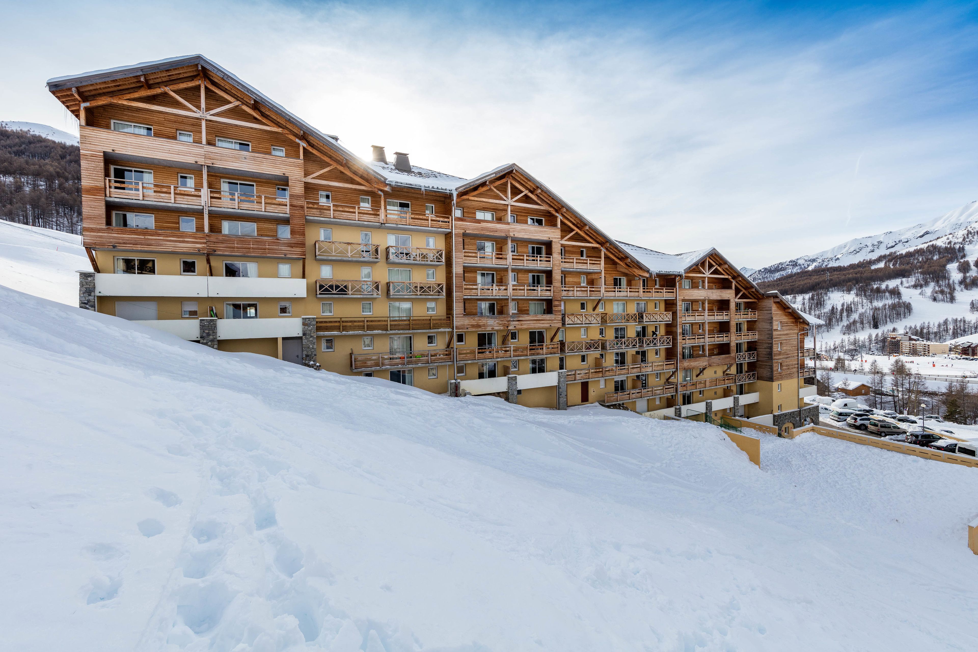 A multi-story wooden building with balconies, set against a snowy mountain backdrop.