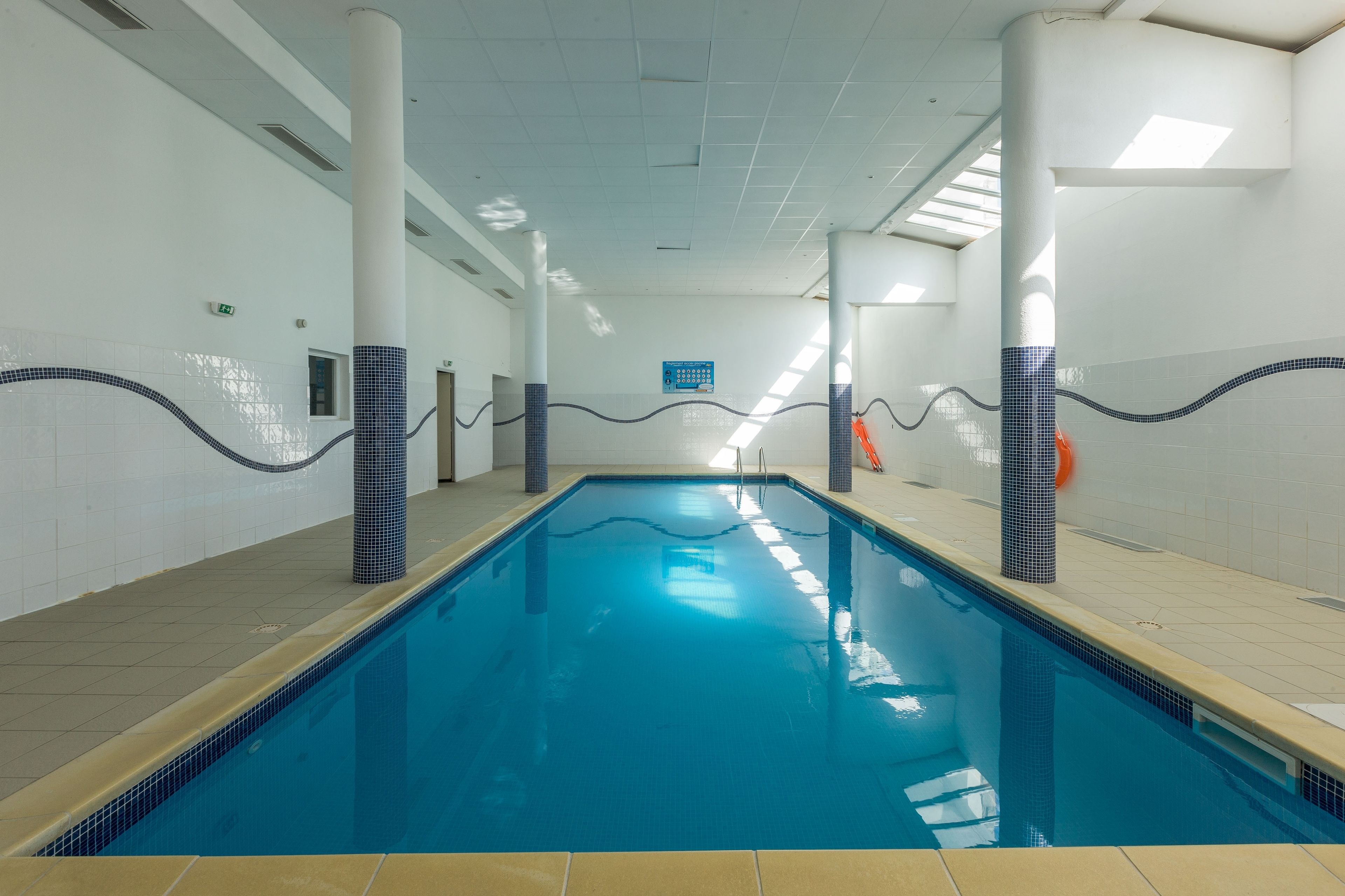 Ein Hallenbad mit klarem, blauen Wasser, gefliesten Wänden und einem gefliesten Boden.