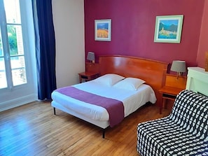 A hotel room with a bed, a chair, a nightstand, a lamp, and a window with curtains.