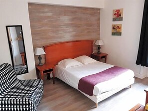 Quarto com cama, poltrona, mesa de cabeceira, luminária e espelho.