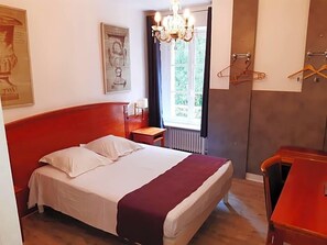 A bedroom with a bed, a nightstand, a dresser, a window with curtains, and a chandelier.