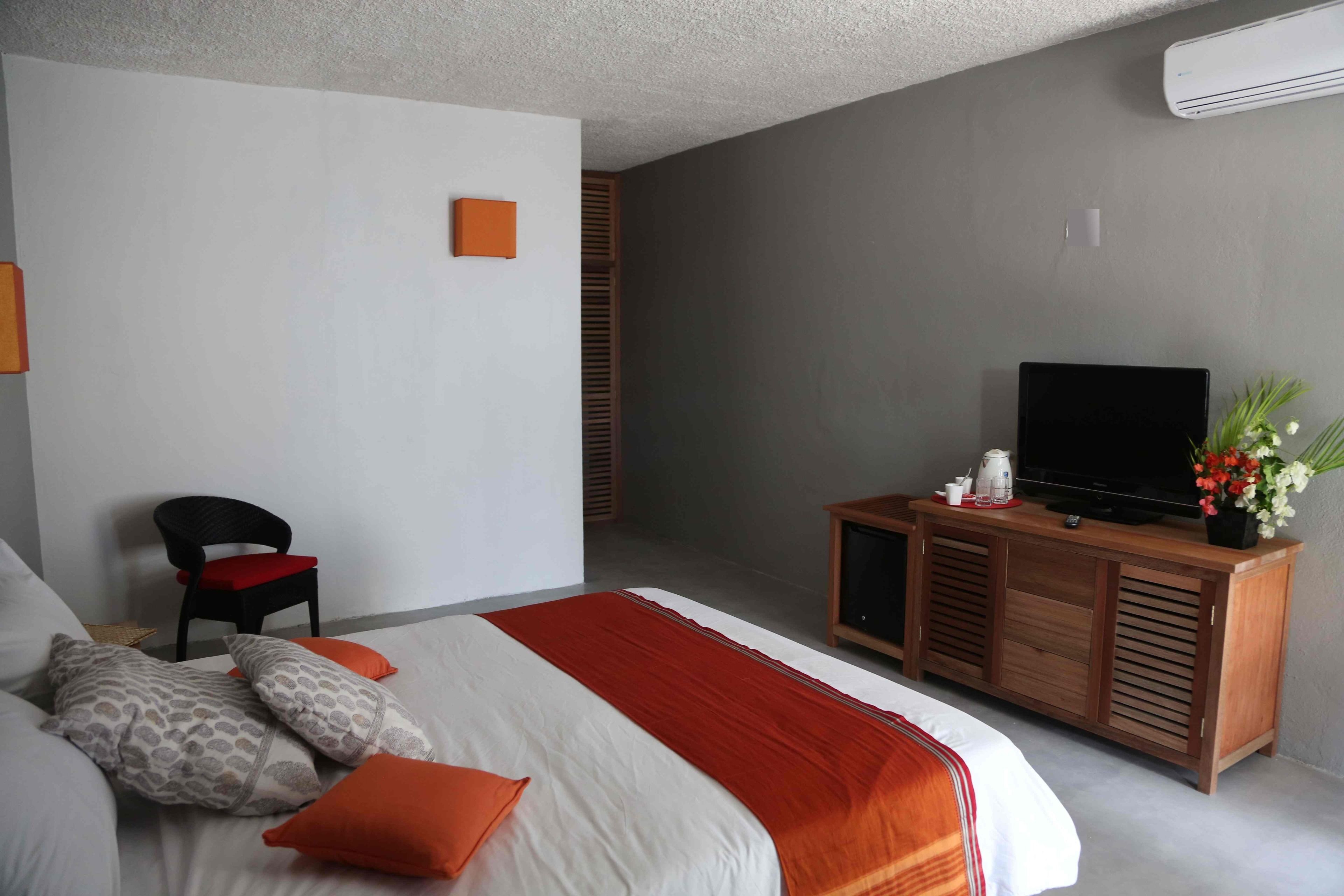 Una habitación de hotel con una cama, un televisor sobre un mueble de madera, una silla y una mesita con un florero.
