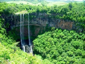 A waterfall cascading into a deep, circular pool surrounded by dense green foliage. - La Tonnelle (Trou aux Biches)