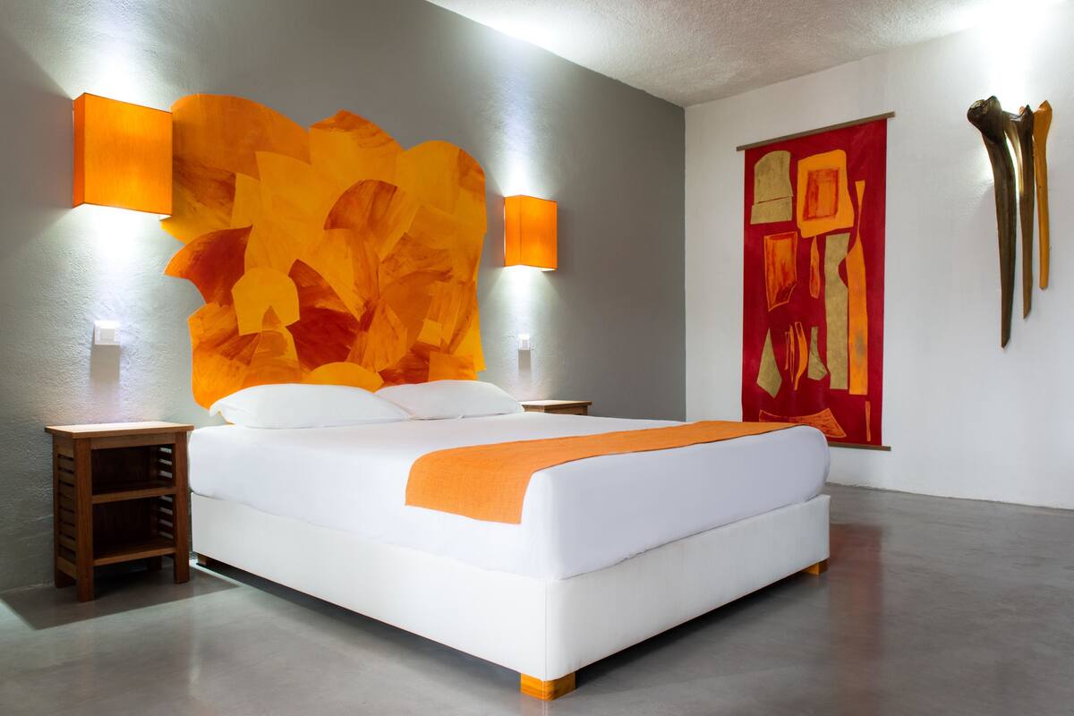 A modern bedroom with a large bed, two bedside tables, a nightstand, and a large abstract painting on the wall.