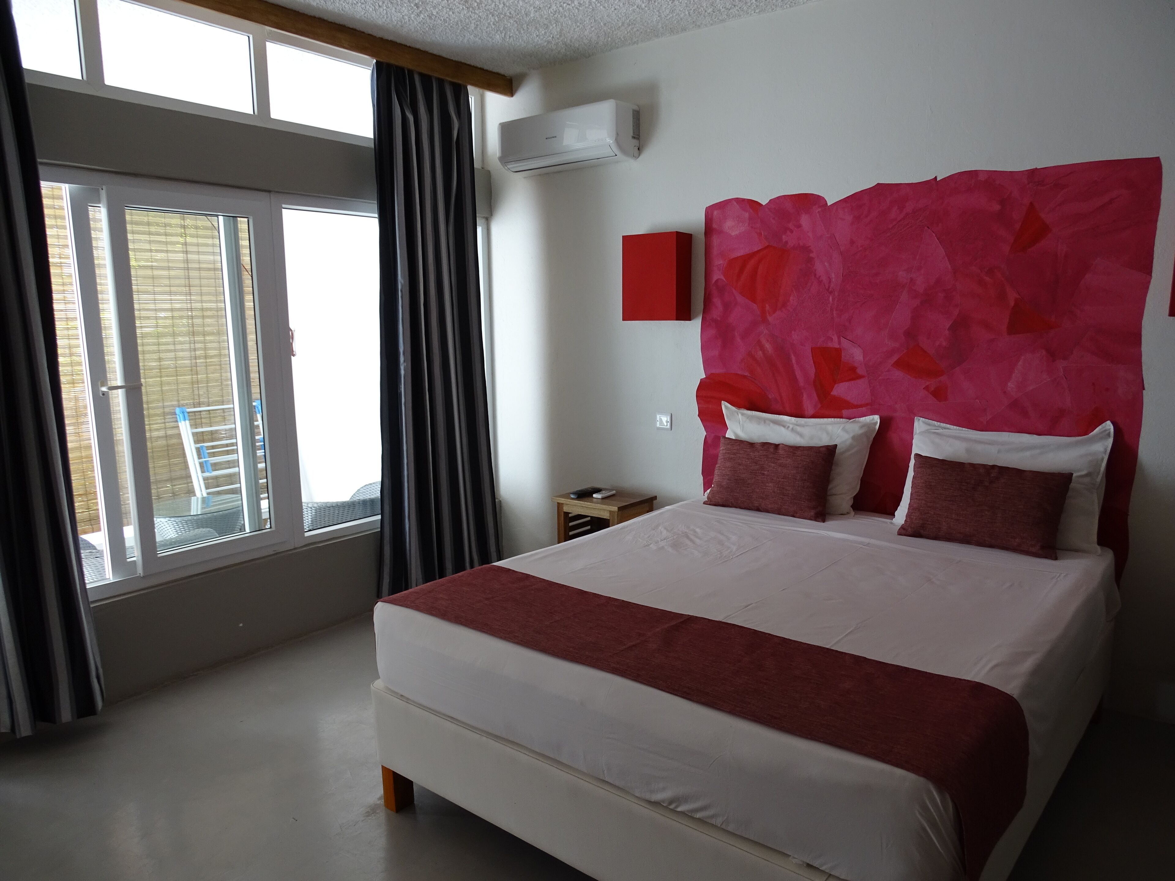 Une chambre d’hôtel avec un grand lit, un mur d’accent rouge et une fenêtre avec des rideaux.