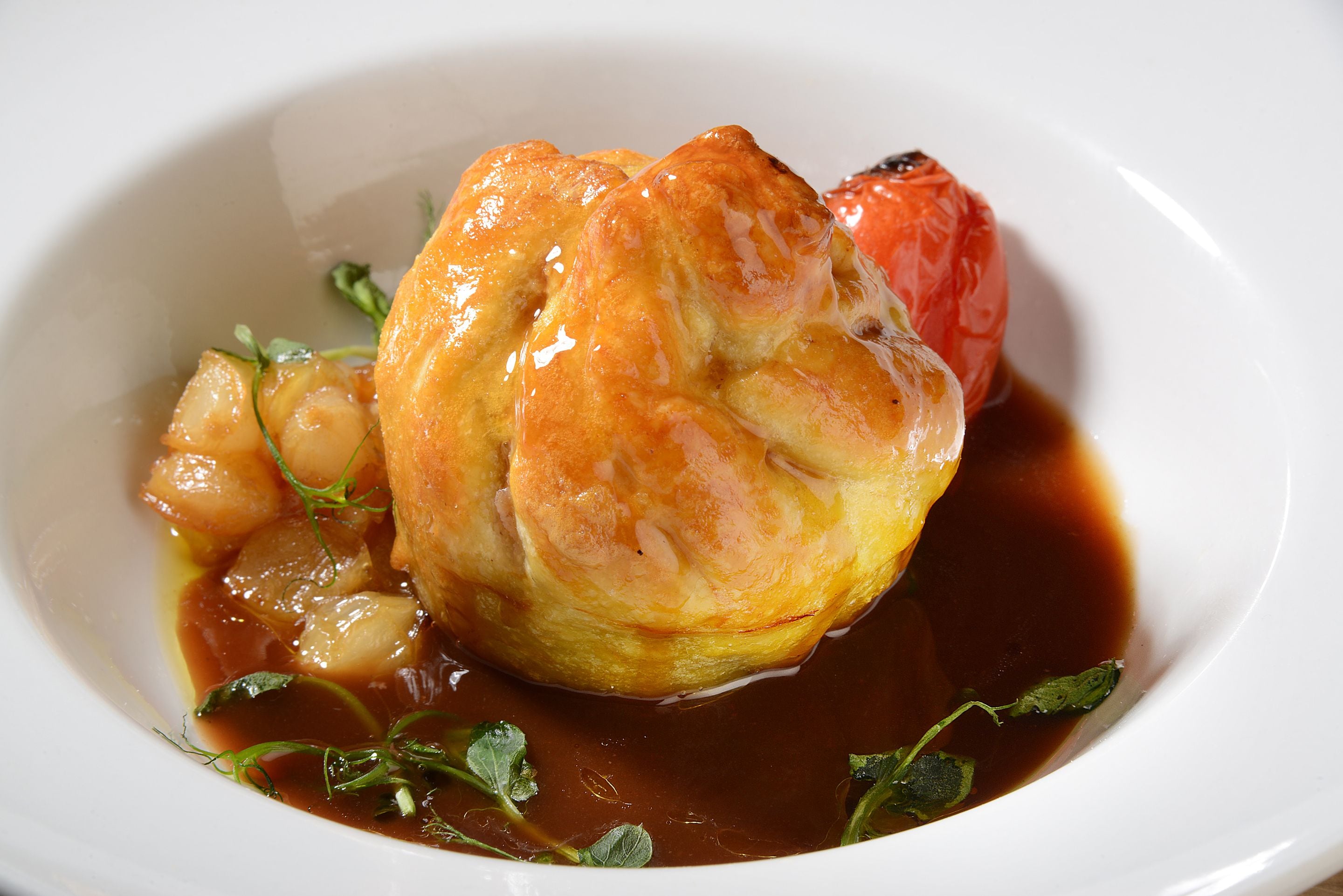 A dish with a pastry, a red fruit, and a sauce on a white plate.