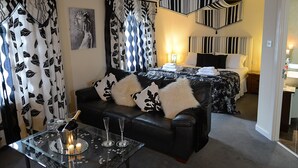 A modern hotel room with a black leather sofa, a glass coffee table with a candle, and a bed with striped curtains. - The Birley Arms Hotel (Preston)