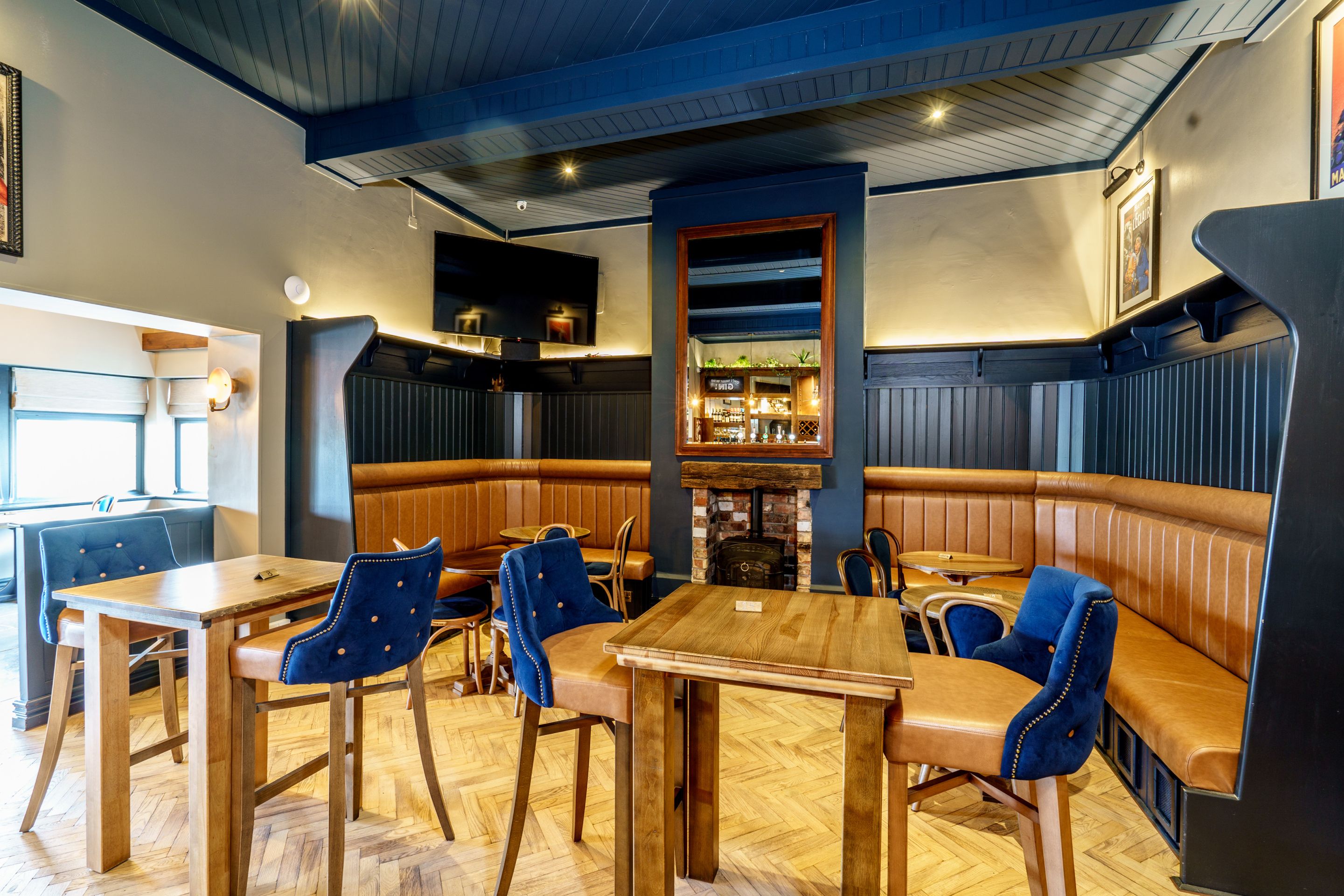 En restaurantindretning med træborde og blåt polstrede stole, en murstenspejs og en bar.