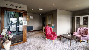 A reception area with a reception desk, a mirror, a red chair, a pink chair, and a small table with a bowl. - The Birley Arms Hotel (Preston)