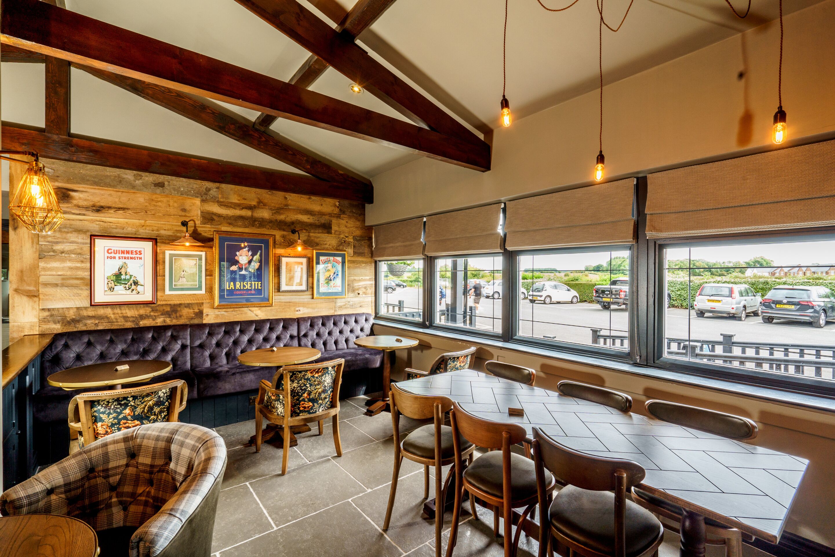 Interior de restaurante con vigas de madera, una zona de bar y vista al estacionamiento a través de amplios ventanales.