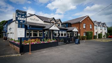 Pub chamado 'The Birley Arms' com área externa para sentar e placa anunciando cervejas em barril e artesanais, produtos frescos da região, café e wifi, além de hospedagem.