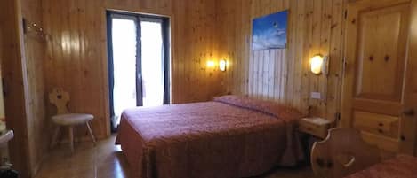 Una habitación con paneles de madera, una cama, una silla, una mesita y una puerta.