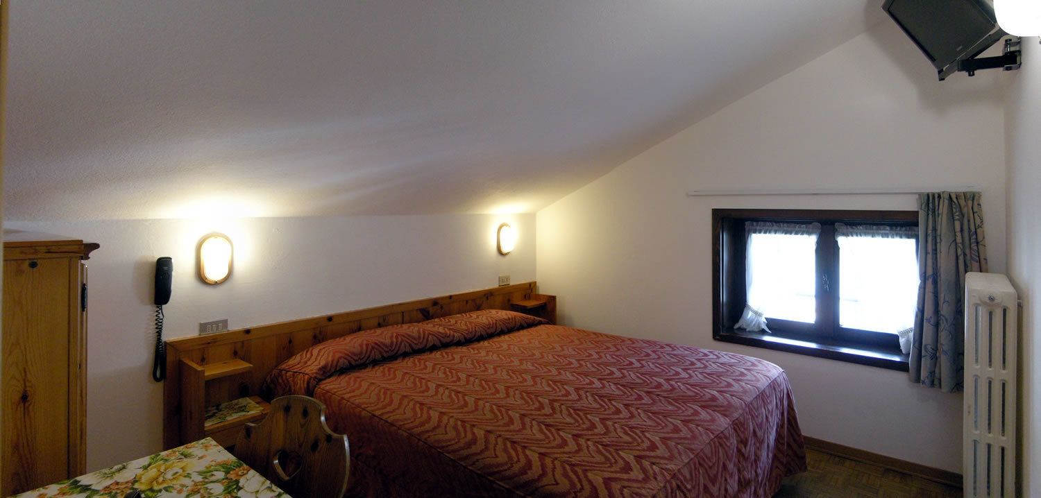 Une chambre à coucher avec un grand lit, un bureau avec une chaise, un téléphone et une fenêtre avec des rideaux.
