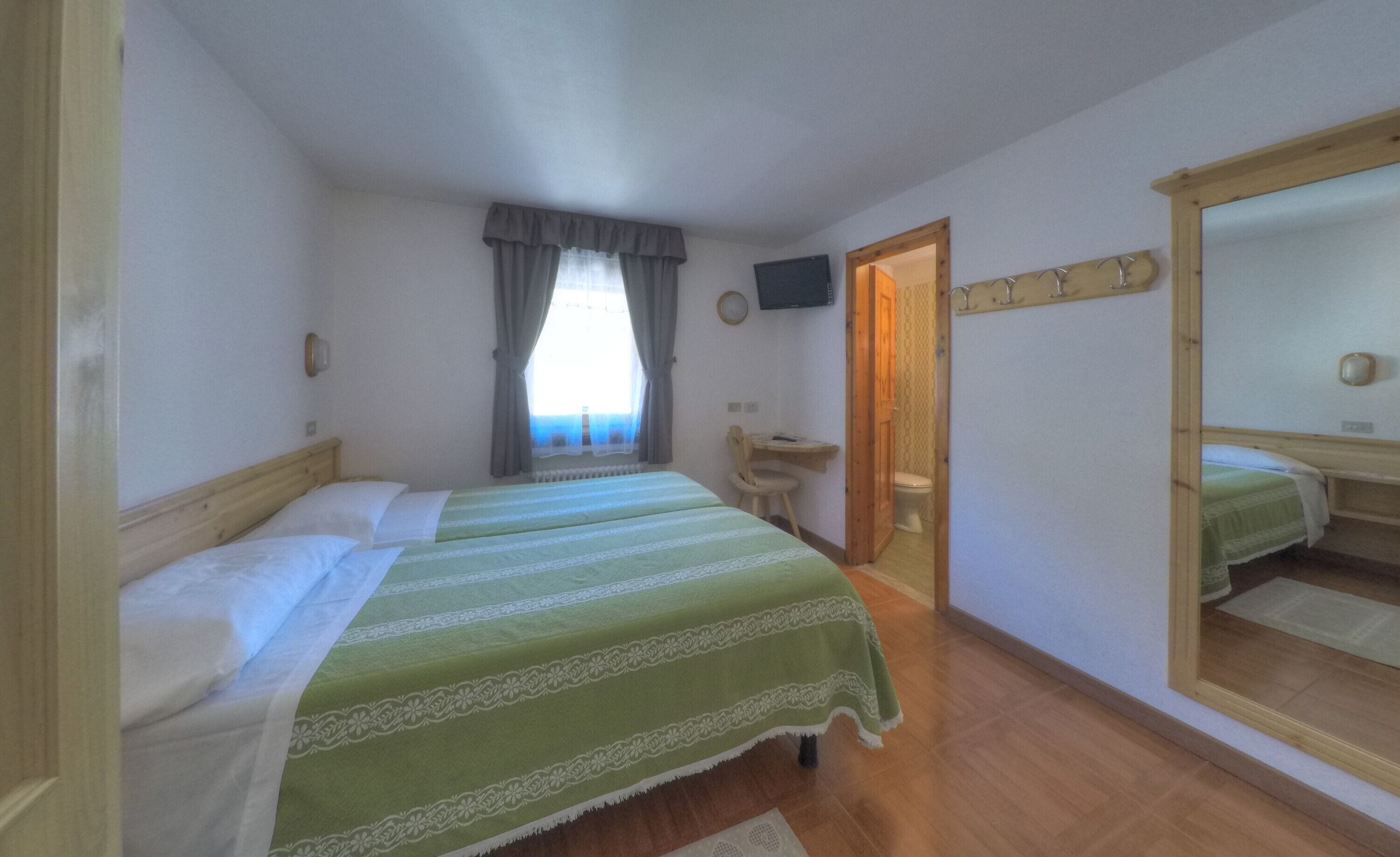 A room with two single beds, a wooden desk, a chair, a mirror, and a television on the wall.