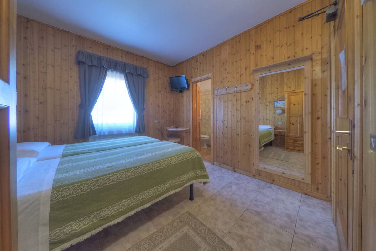 Ein Zimmer mit Holzwänden, einem Bett, einem Fernseher und einem durch eine Tür einsehbaren Badezimmer.