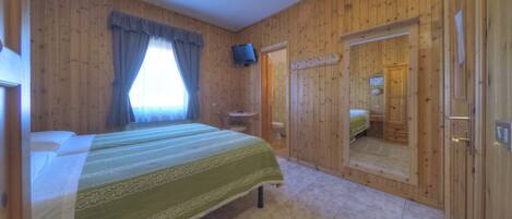 A wooden-paneled room with a bed, a television, and a bathroom visible through a door.