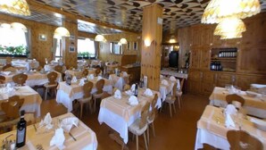 A restaurant with multiple tables set for dining, wooden paneling on the walls, and hanging pendant lights. - Hotel Ristorante Federia (Livigno)