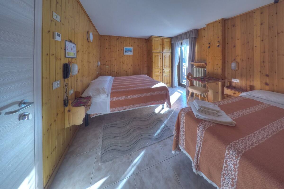 Ein Zimmer mit Holzwänden und Fliesenboden, ausgestattet mit zwei Betten, einem Schreibtisch und einem Stuhl.