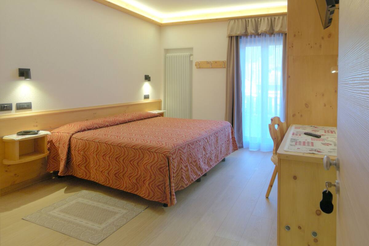 Ein Schlafzimmer mit Bett, Nachttischen, einem Holzschrank, einem Fenster mit Vorhängen und einer Tür.