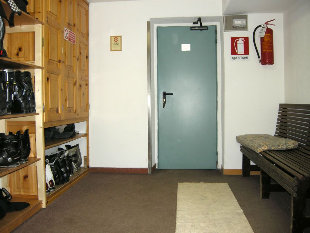 Una habitación con una puerta azul verdosa, un extintor, un banco y estantes con cascos.