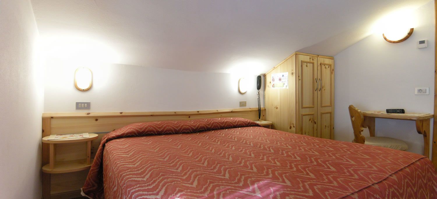 Habitación de hotel con cama, escritorio, silla, armario y mesita de noche.