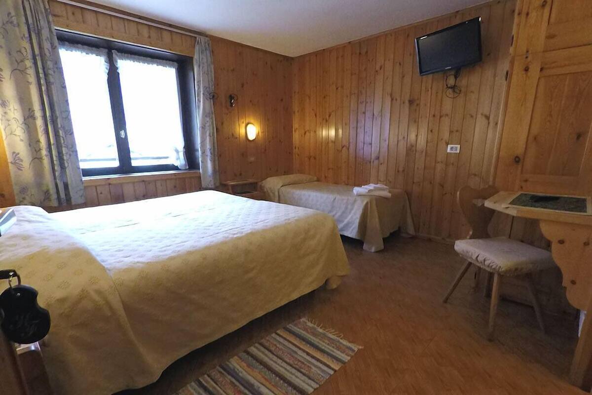 Ein Zimmer aus Holz mit zwei Betten, einem Sessel, einem Fernseher und einem Fenster mit Vorhängen.