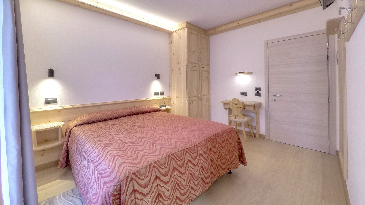Een slaapkamer met een bed, nachtkastjes, een stoel, een kledingkast en een deur.
