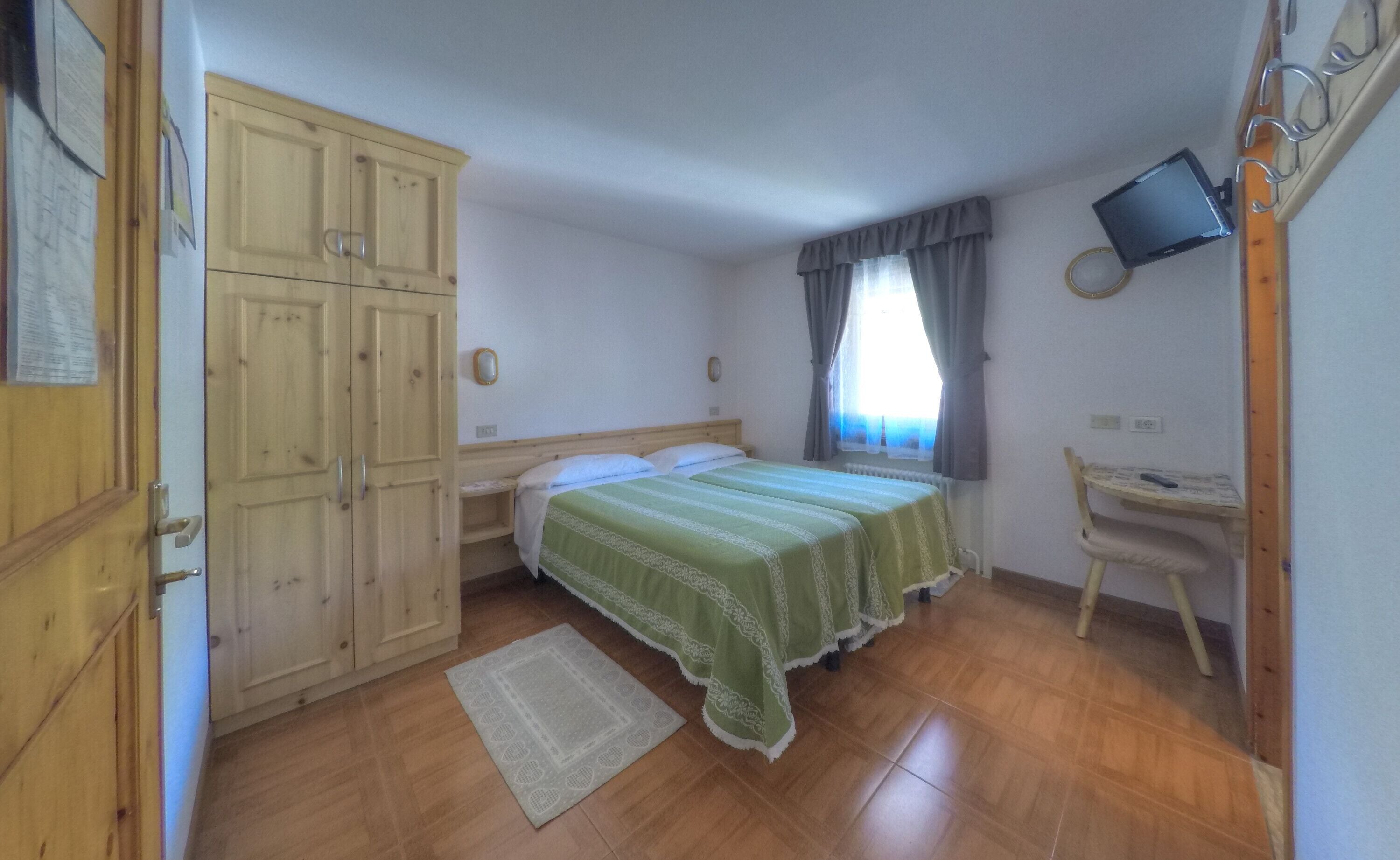 A bedroom with two beds, wooden wardrobe, a desk, a television, and a window with curtains.