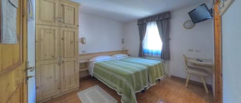 A bedroom with two beds, wooden wardrobe, a desk, a television, and a window with curtains.