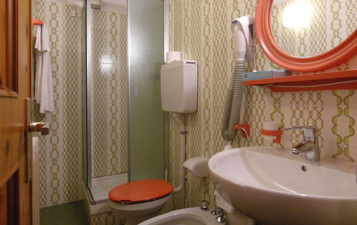 Un baño con inodoro, lavamanos y secador de pelo fijado a la pared.