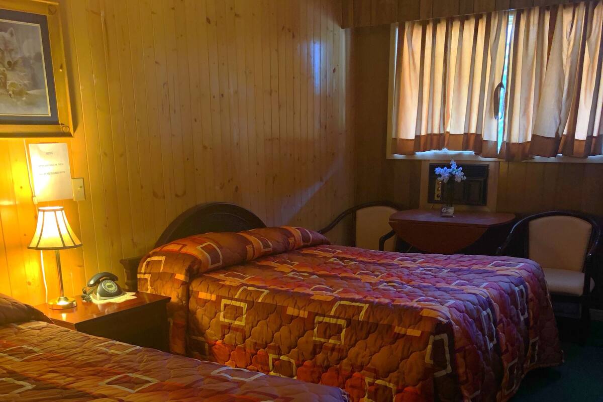 A hotel room with two beds, a desk, a chair, a lamp, and a window with curtains.