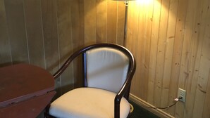 A wooden-paneled room with a wooden chair and a table. A lamp is on the wall. - Alta Vista Motel (Baldwin)