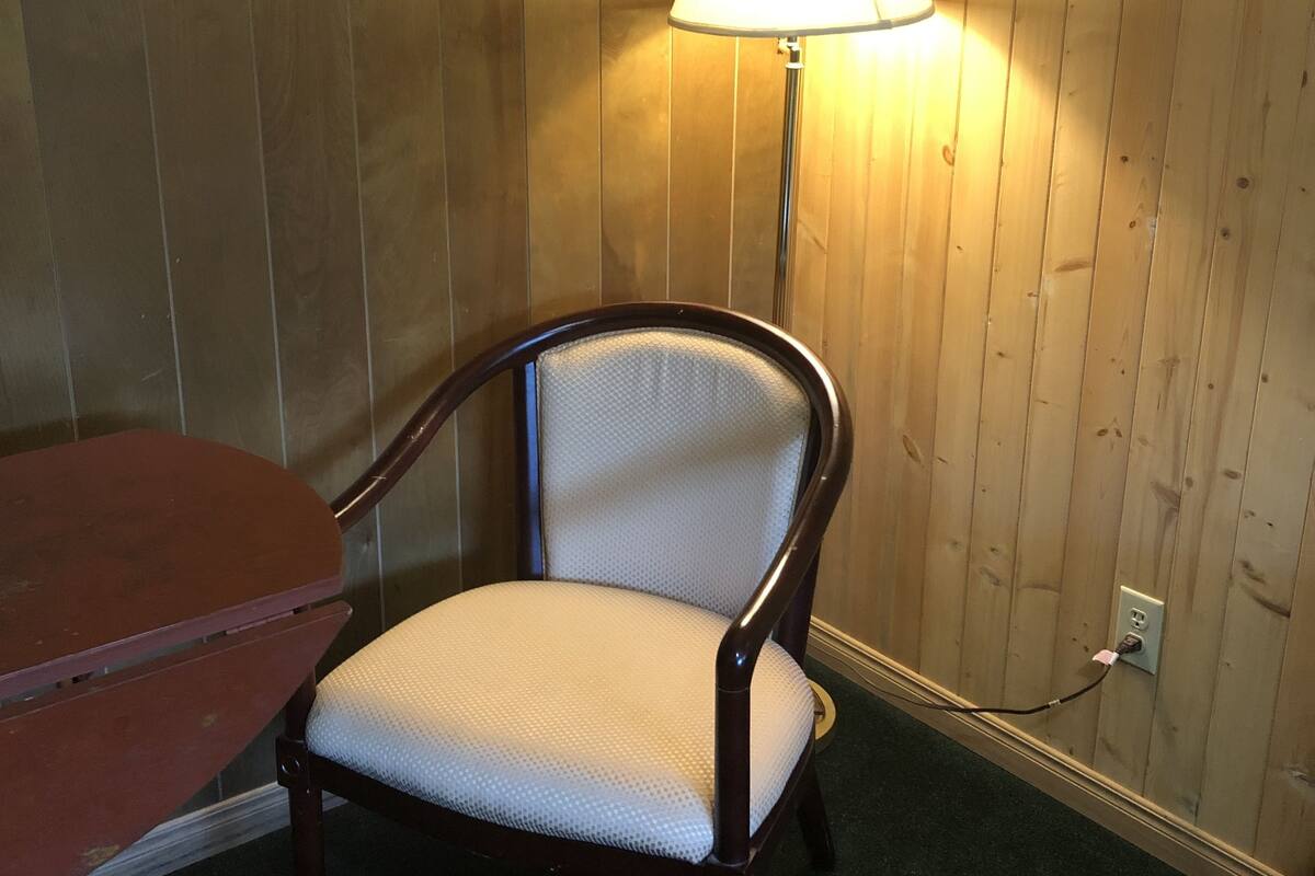 A wooden-paneled room with a wooden chair and a table. A lamp is on the wall.