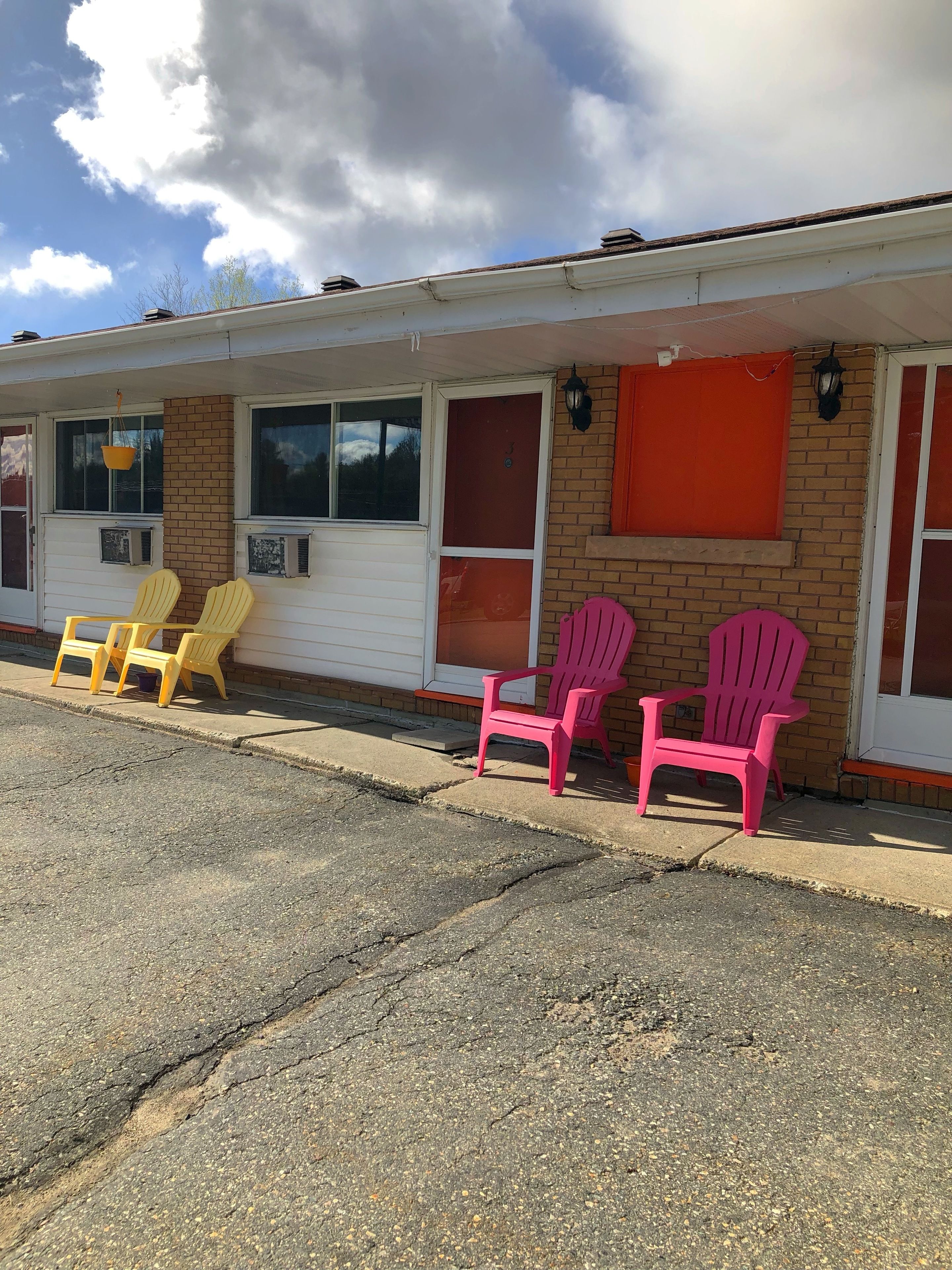 Um motel com duas fileiras de cadeiras na frente, fachada de tijolos e céu claro.