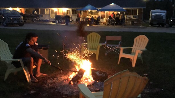 A campfire with chairs around it, a building in the background, and a vehicle parked nearby. - Alta Vista Motel (Baldwin)