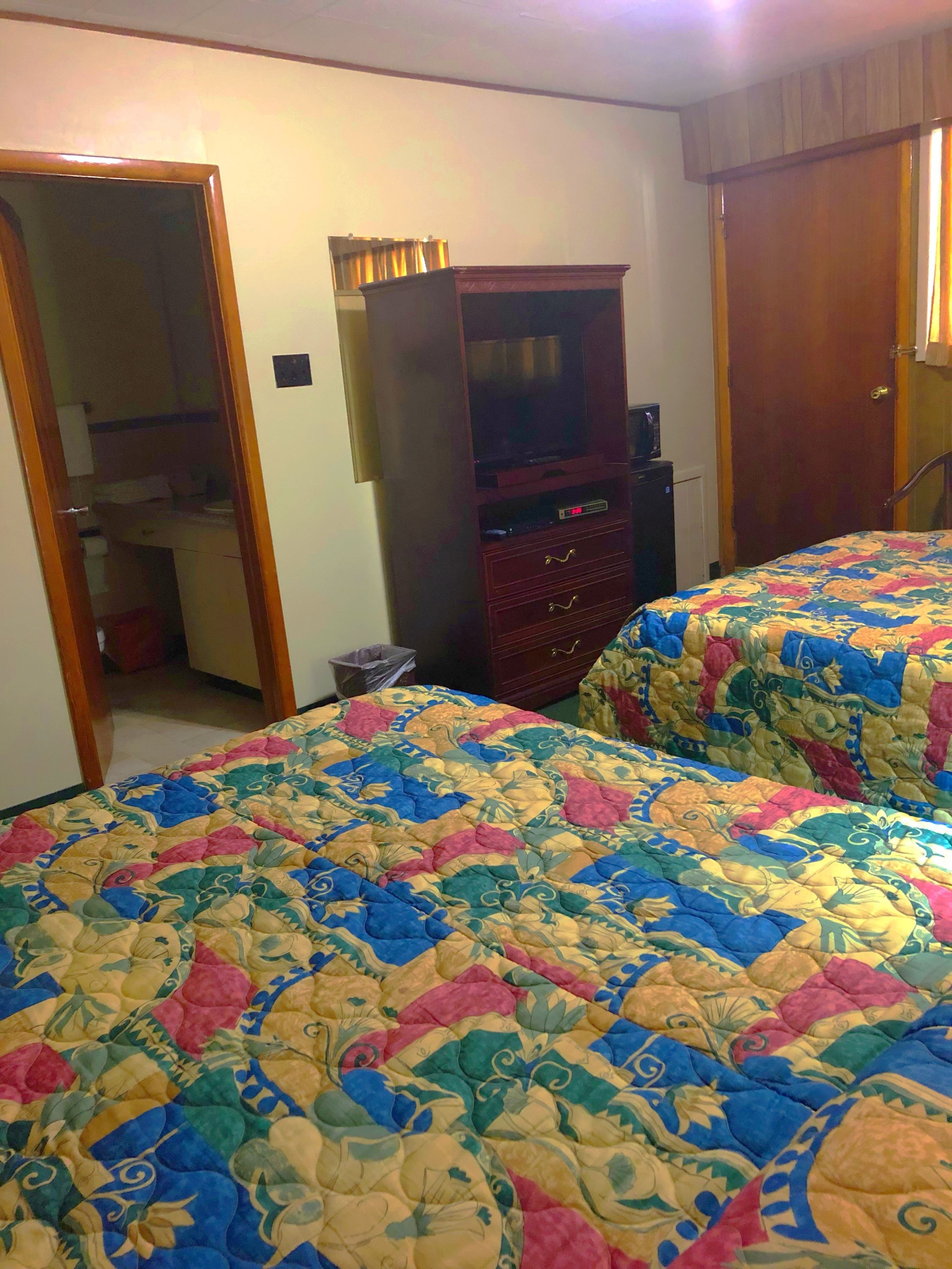 A bedroom with two beds, a wooden wardrobe, and a television.