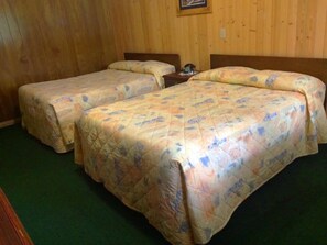 Una habitación con dos camas, paredes de madera y una alfombra verde.