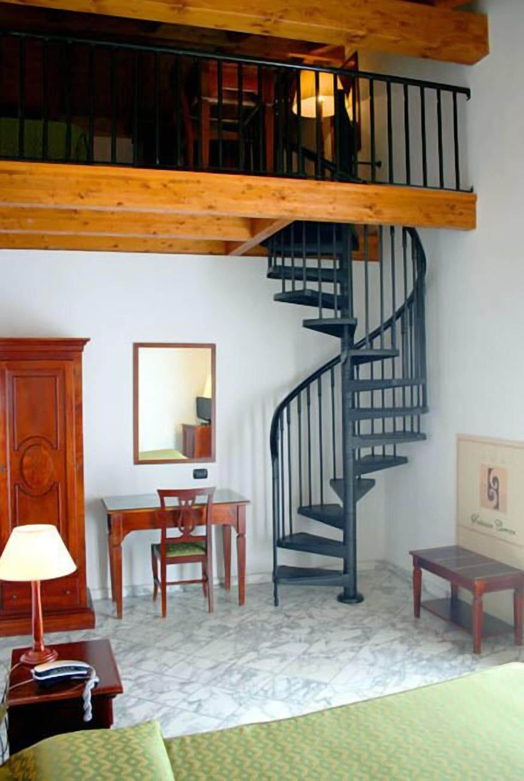 A room with a wooden staircase, a desk with a chair, a cabinet, and a bed.