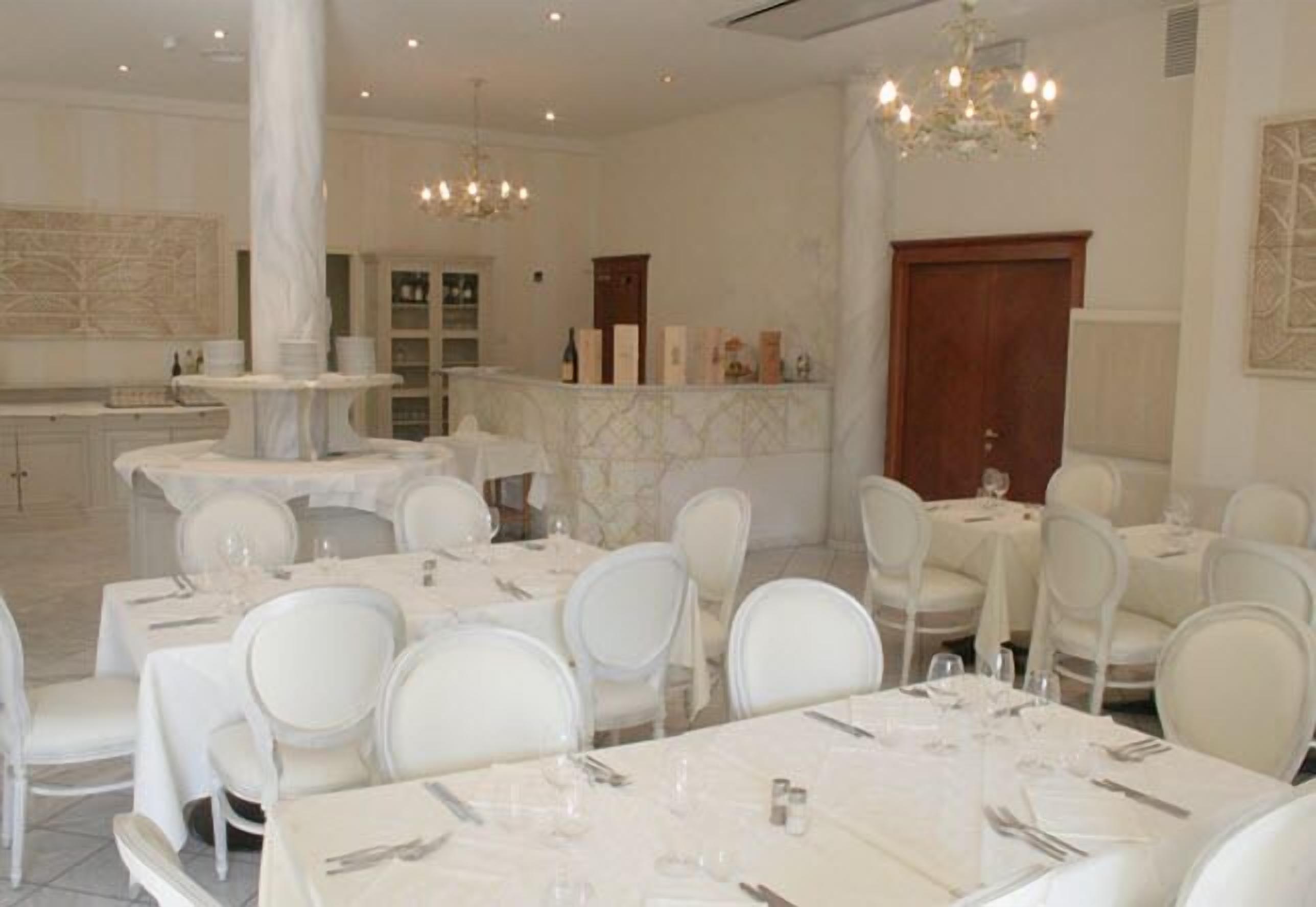 A dining area with white tables and chairs, marble flooring, and chandeliers.