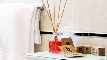 A bathroom counter with a white towel, a glass bottle of red liquid, reed diffusers, and several small brown boxes.
