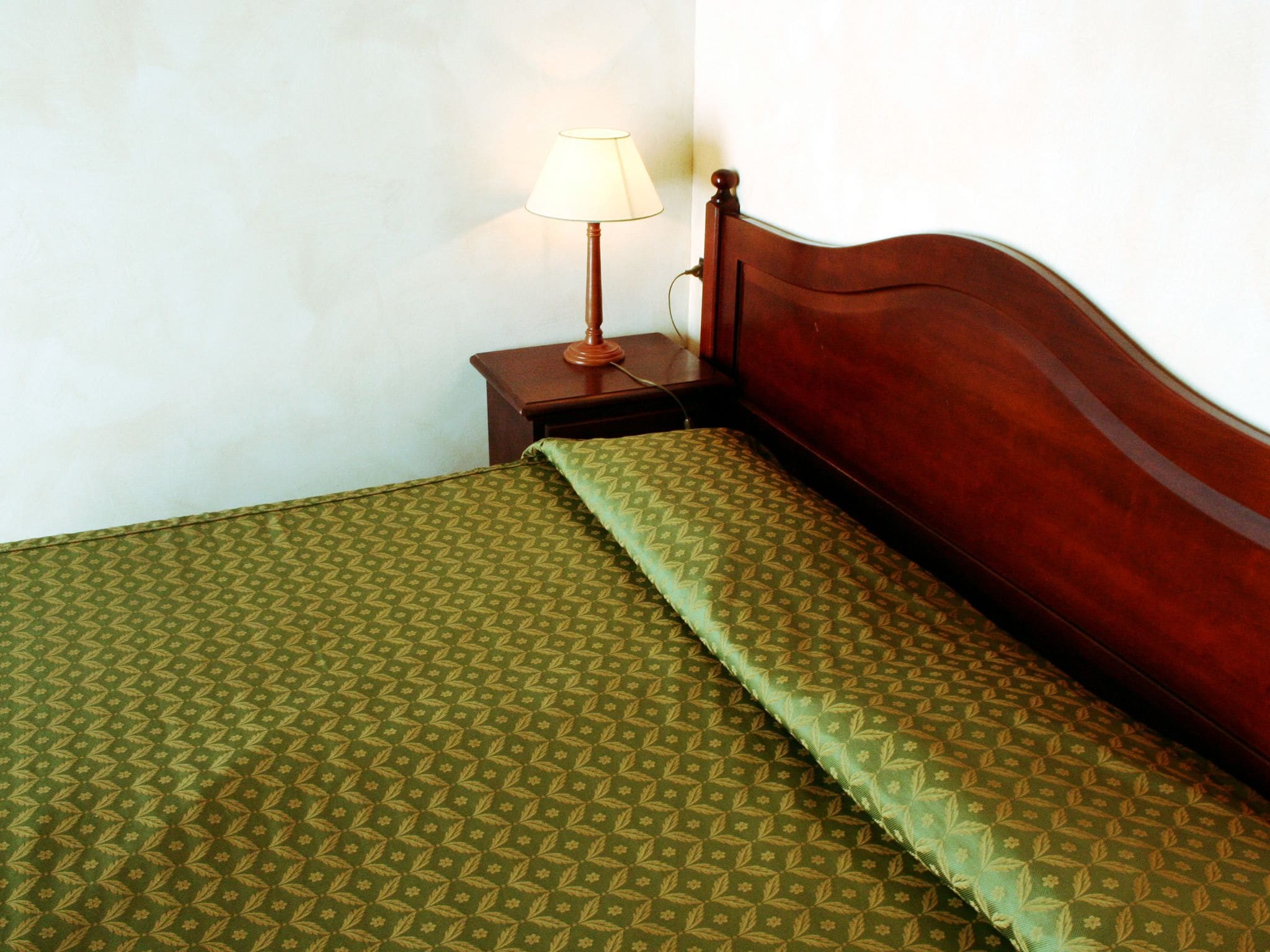 Una cama bien hecha con una colcha verde estampada y un cabecero de madera.