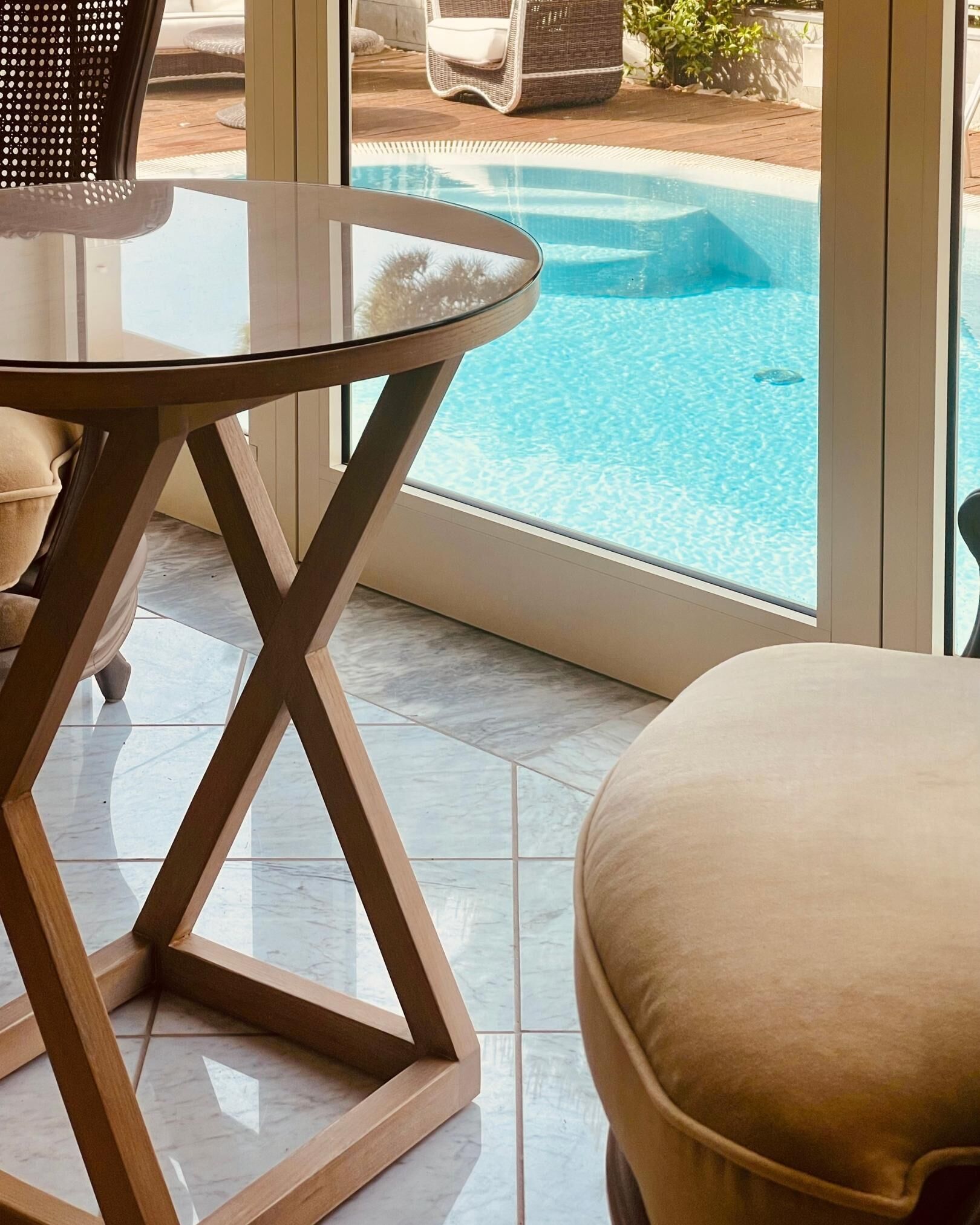 Een modern binnenzwembad met een glazen tafel en beige zitplaatsen.