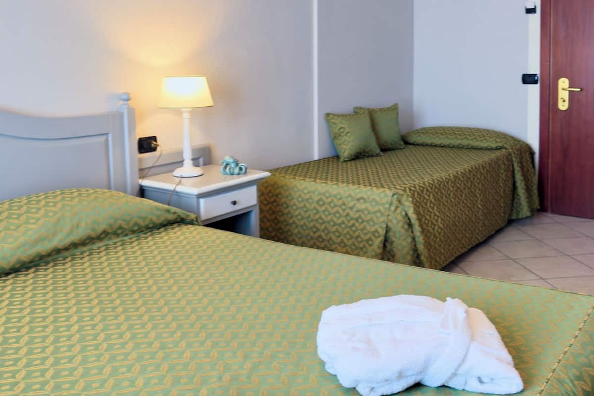 A hotel room with two beds, a nightstand with a lamp, and a door.