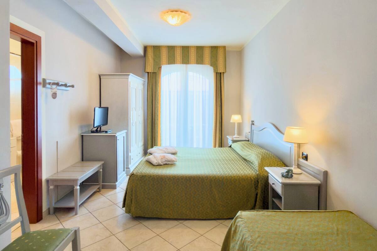 A hotel room with two beds, a desk, a chair, a TV, and a window with curtains.