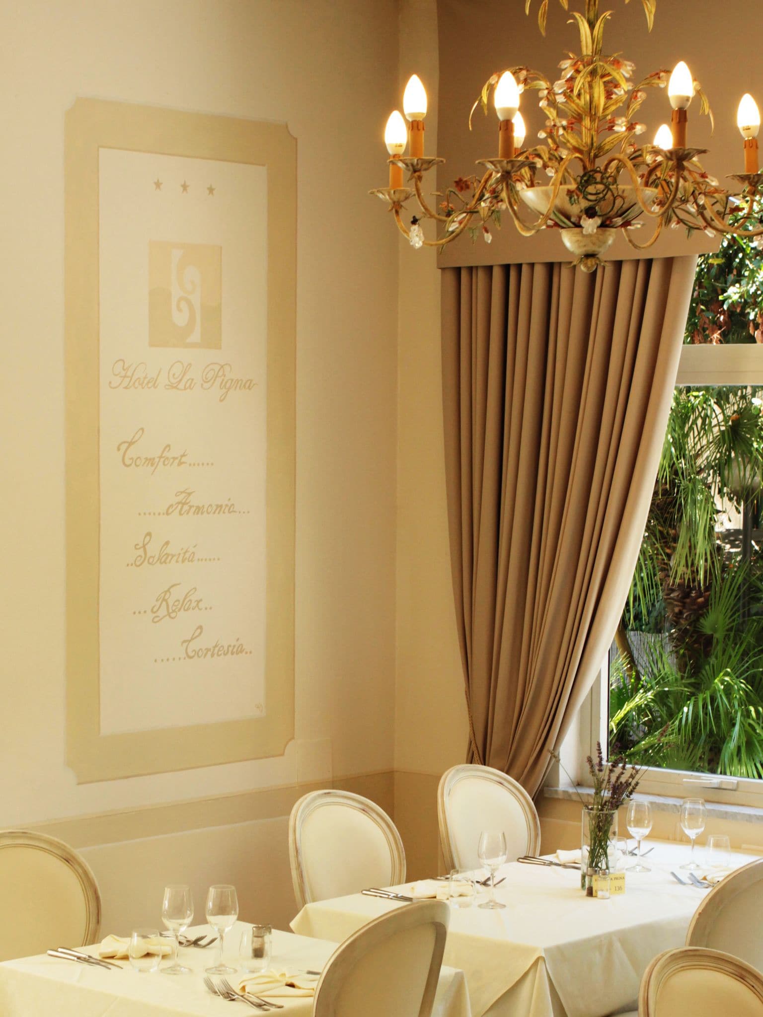 A dining area with a chandelier, a menu on the wall, and a view of greenery outside.