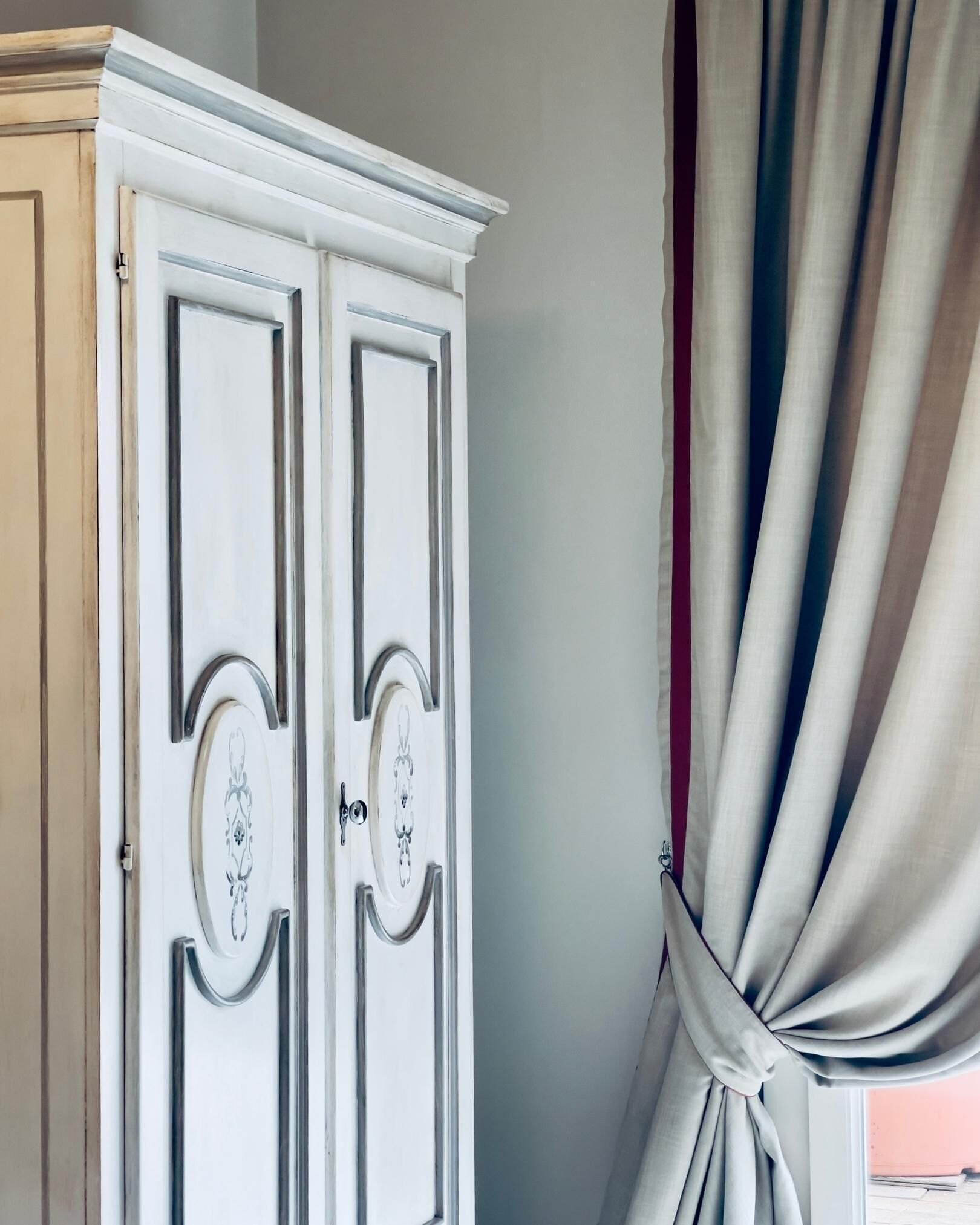 A white wardrobe with ornate handles and a door with a decorative panel.