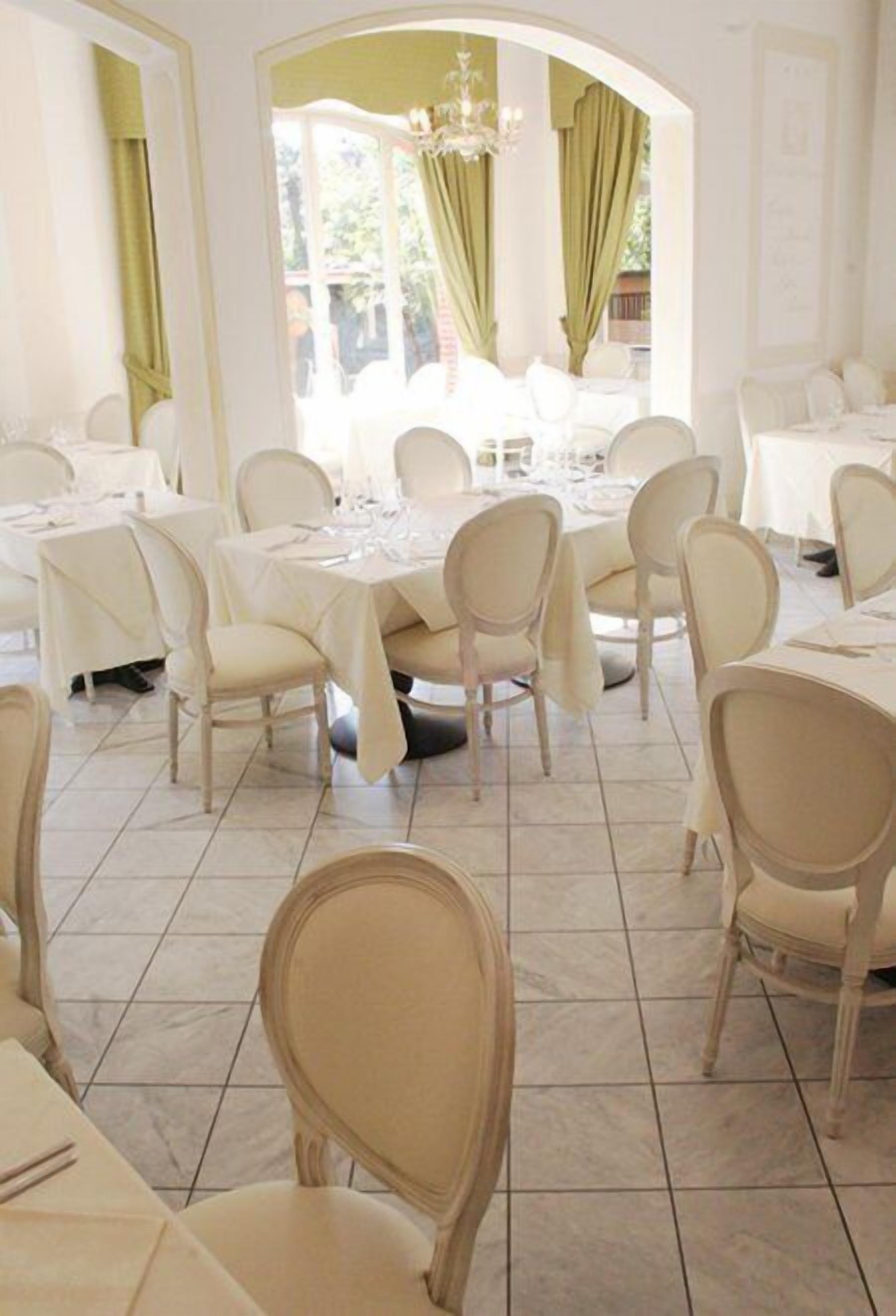 Un comedor con mesas y sillas redondas, una araña y vistas a través de un gran ventanal.