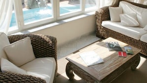 Une pièce meublée de meubles en osier, avec une table basse en bois et une vue sur une piscine.