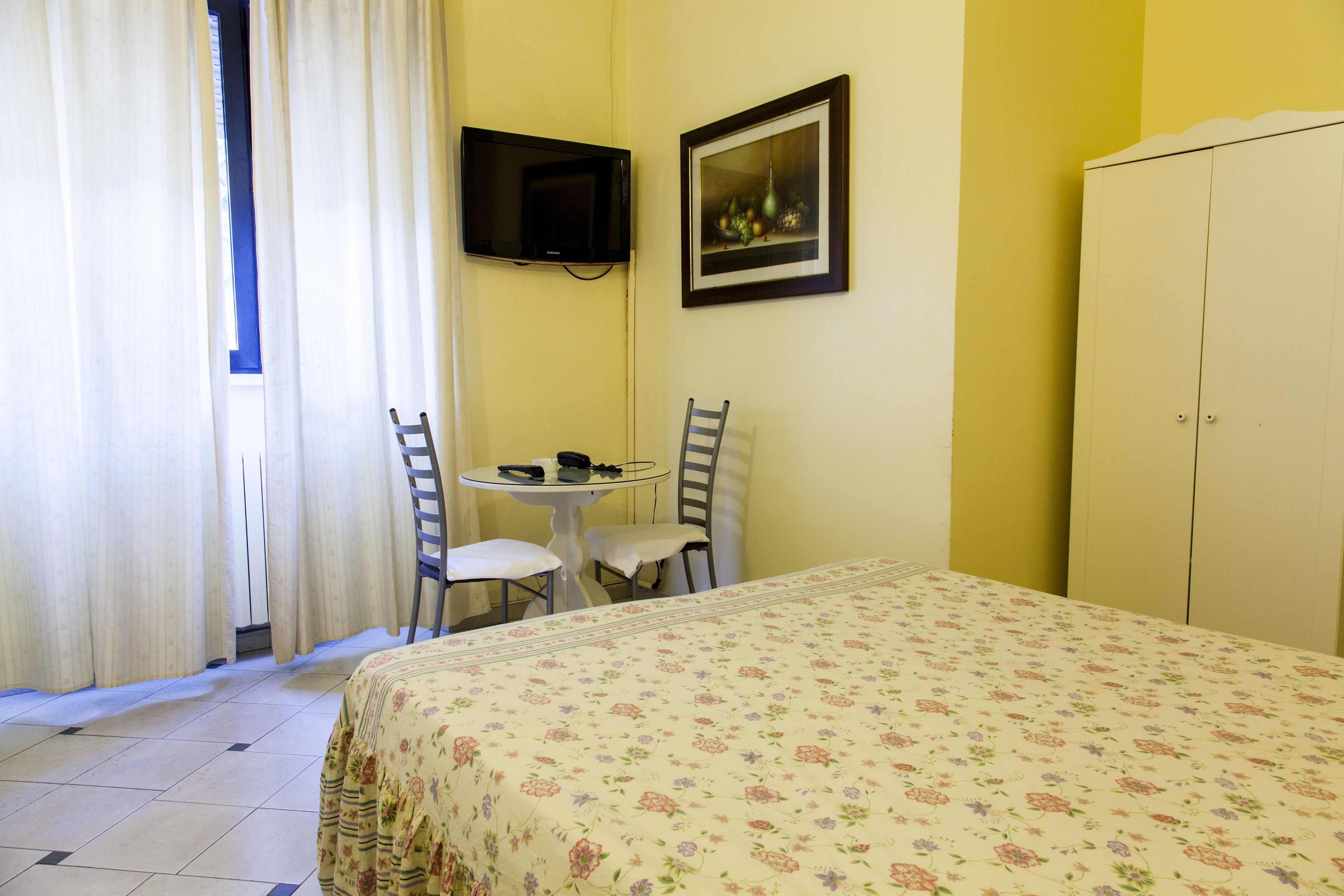 Una habitación con cama, una mesa con sillas, televisión y armario.